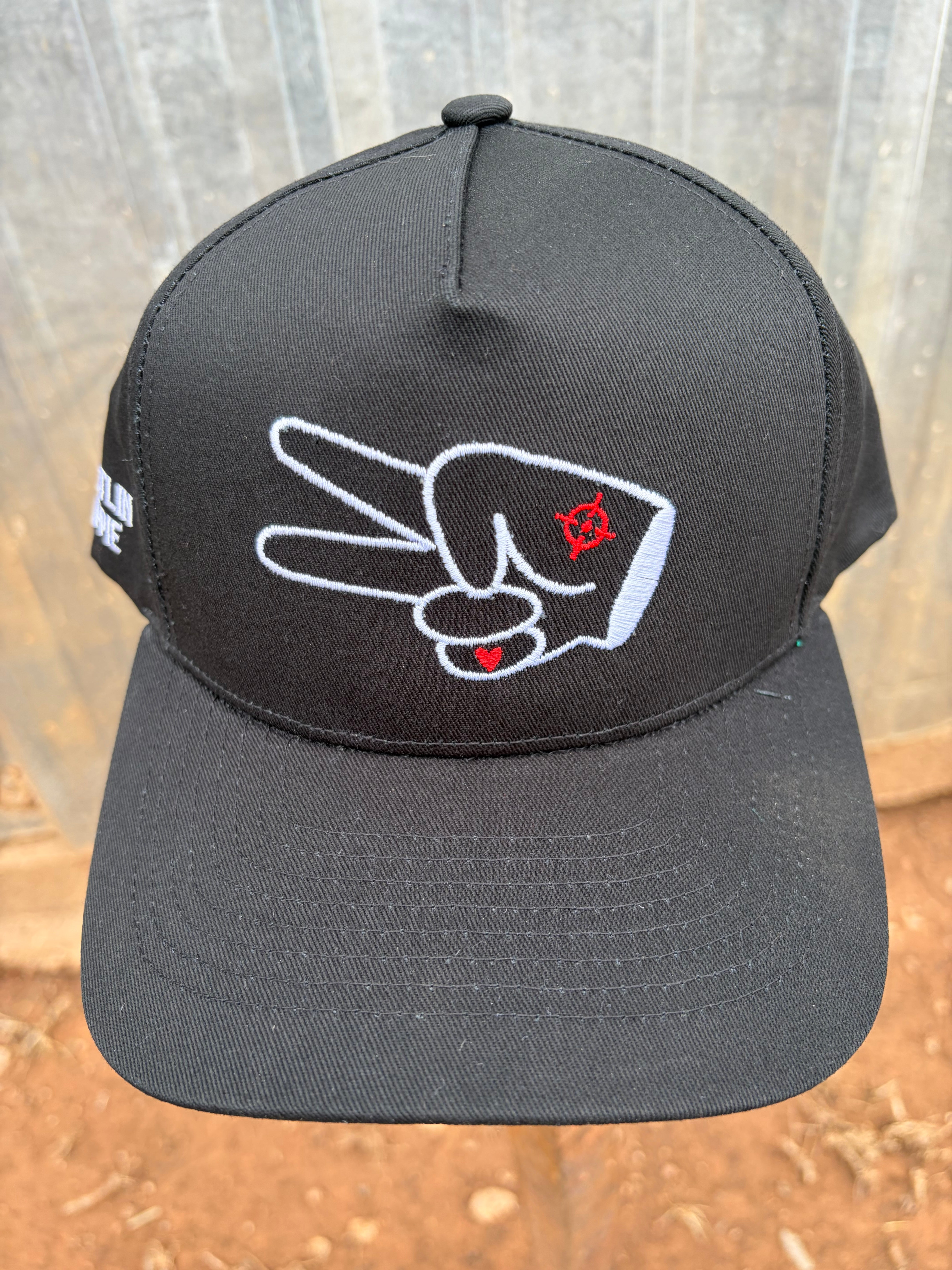 Front-facing close-up of black Hustlin Hippie curved snapback hat with large embroidered peace hand logo in white and red stitching on structured crown