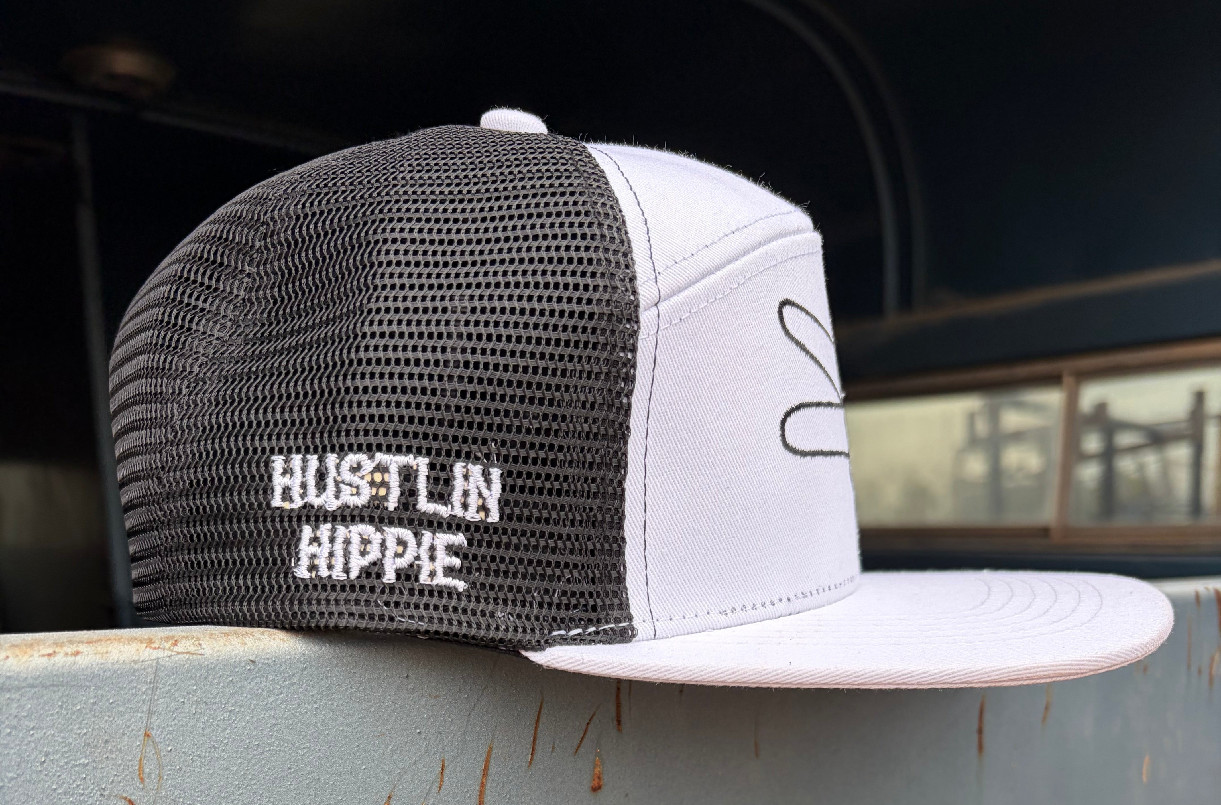 Side view of a white and black Hustlin Hippie mesh trucker snapback hat featuring embroidered side branding and breathable black mesh backing.