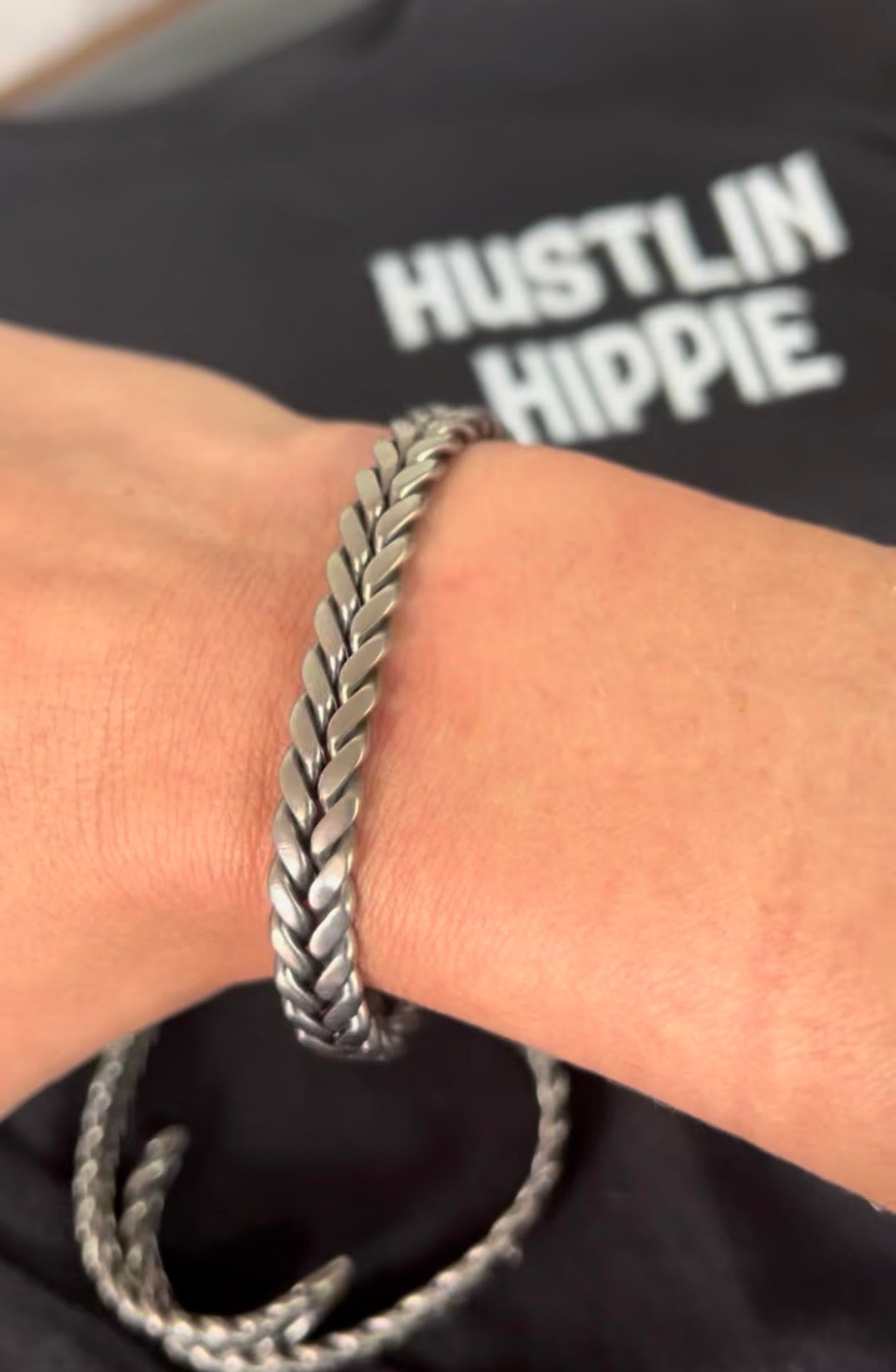 Handmade 316 stainless steel cuff bracelet worn on wrist with Hustlin Hippie apparel background