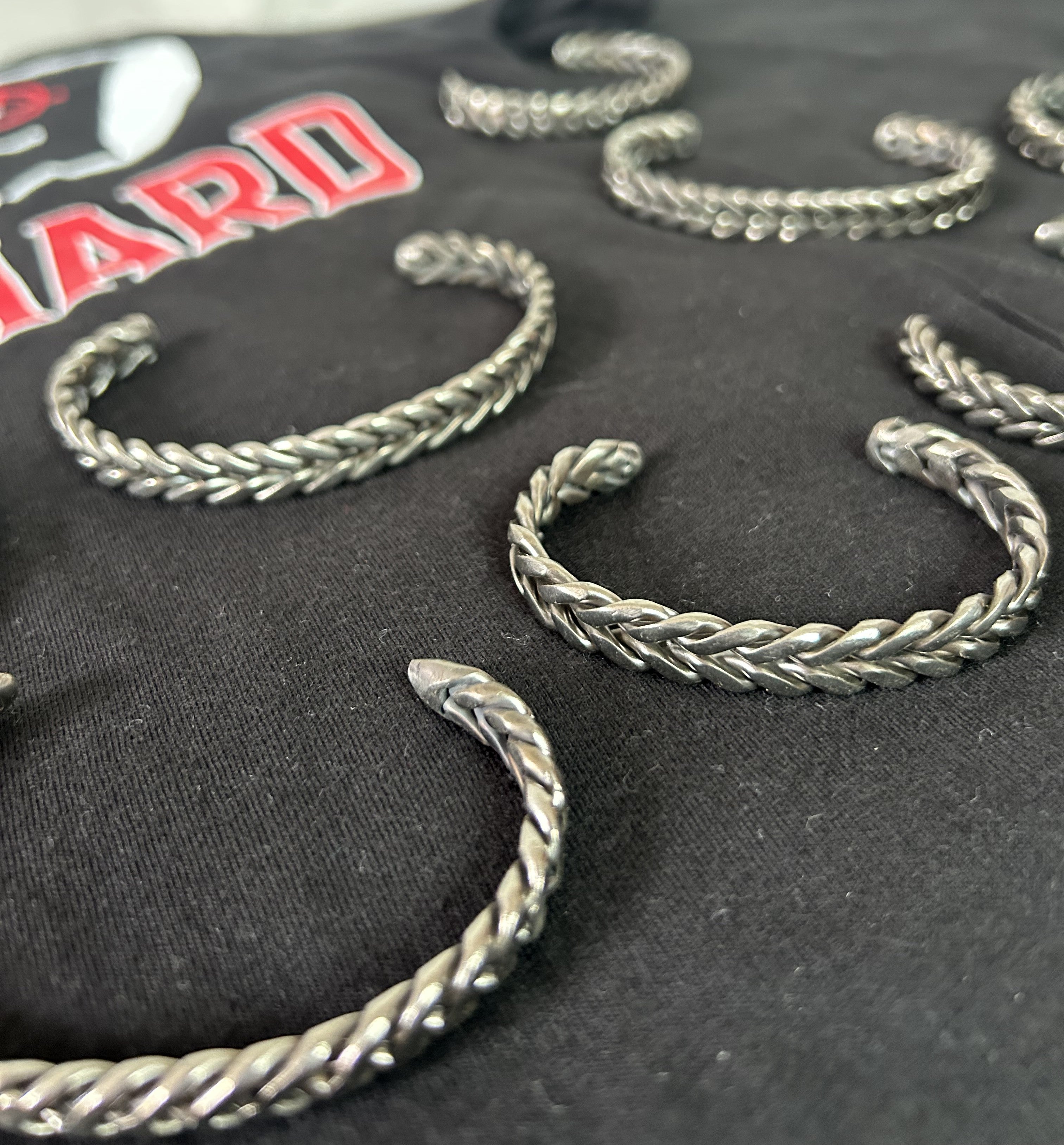 Collection of handmade 316 stainless steel bracelets displayed on Hustlin Hippie shirt