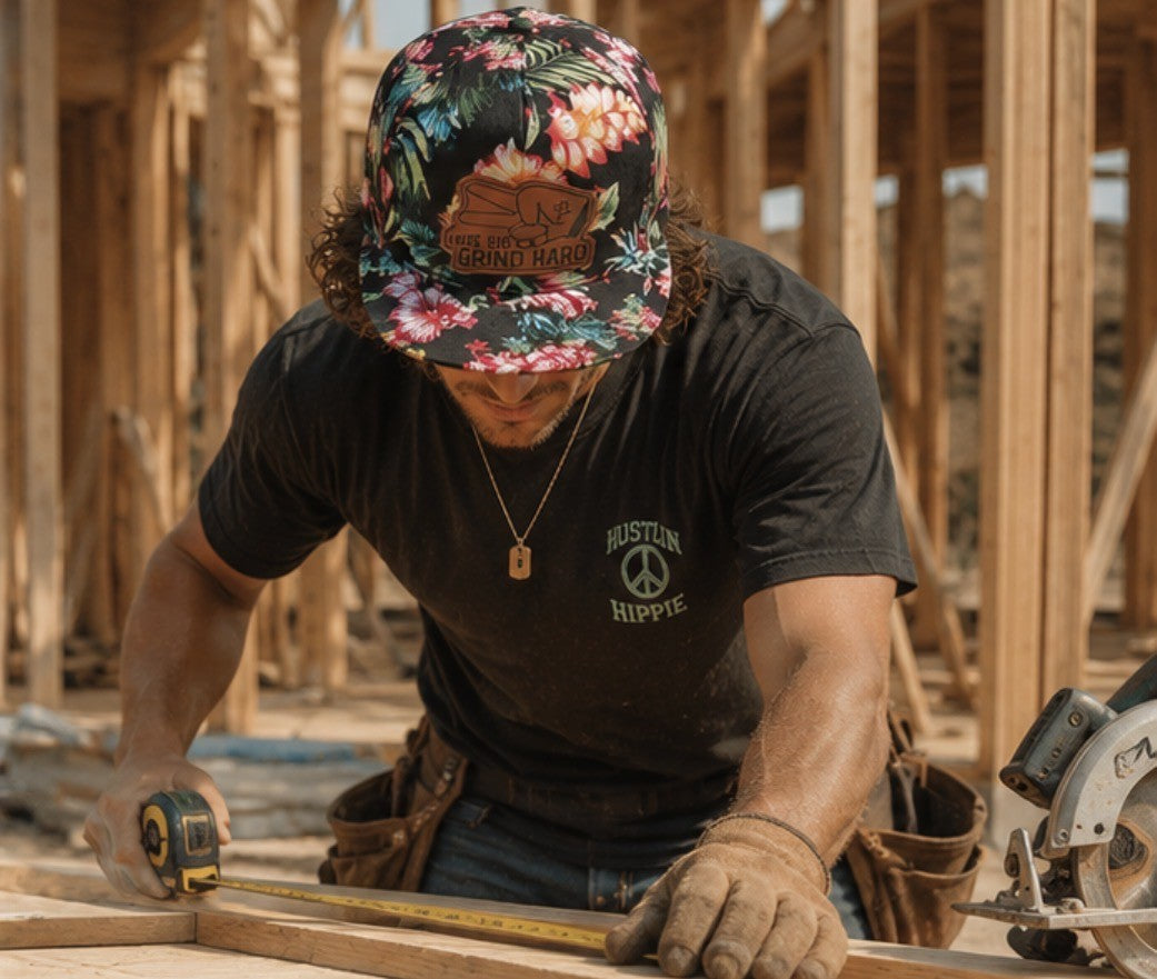 Man wearing Hustlin Hippie floral 5 panel snapback hat working on framing construction jobsite with measuring tape
