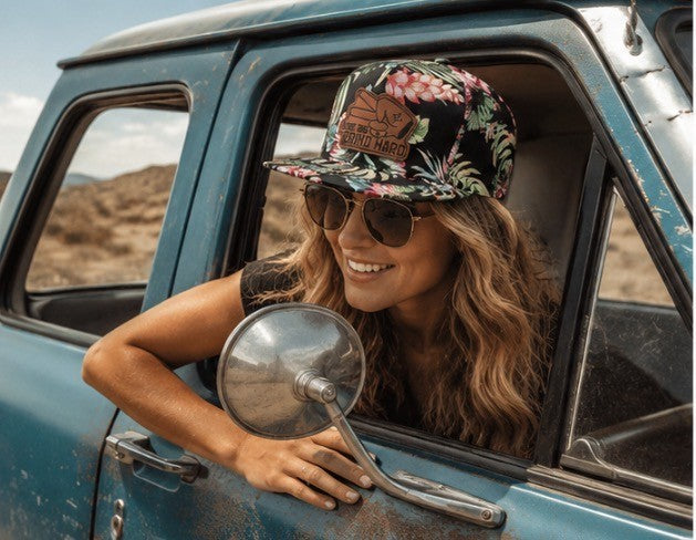 Woman wearing floral Hustlin Hippie snapback hat with leather Love Big Grind Hard patch leaning out vintage truck window