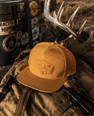 Hustlin Hippie hydro snapback displayed with hunting gear and antlers in an outdoor campsite setting with rustic adventure vibes.