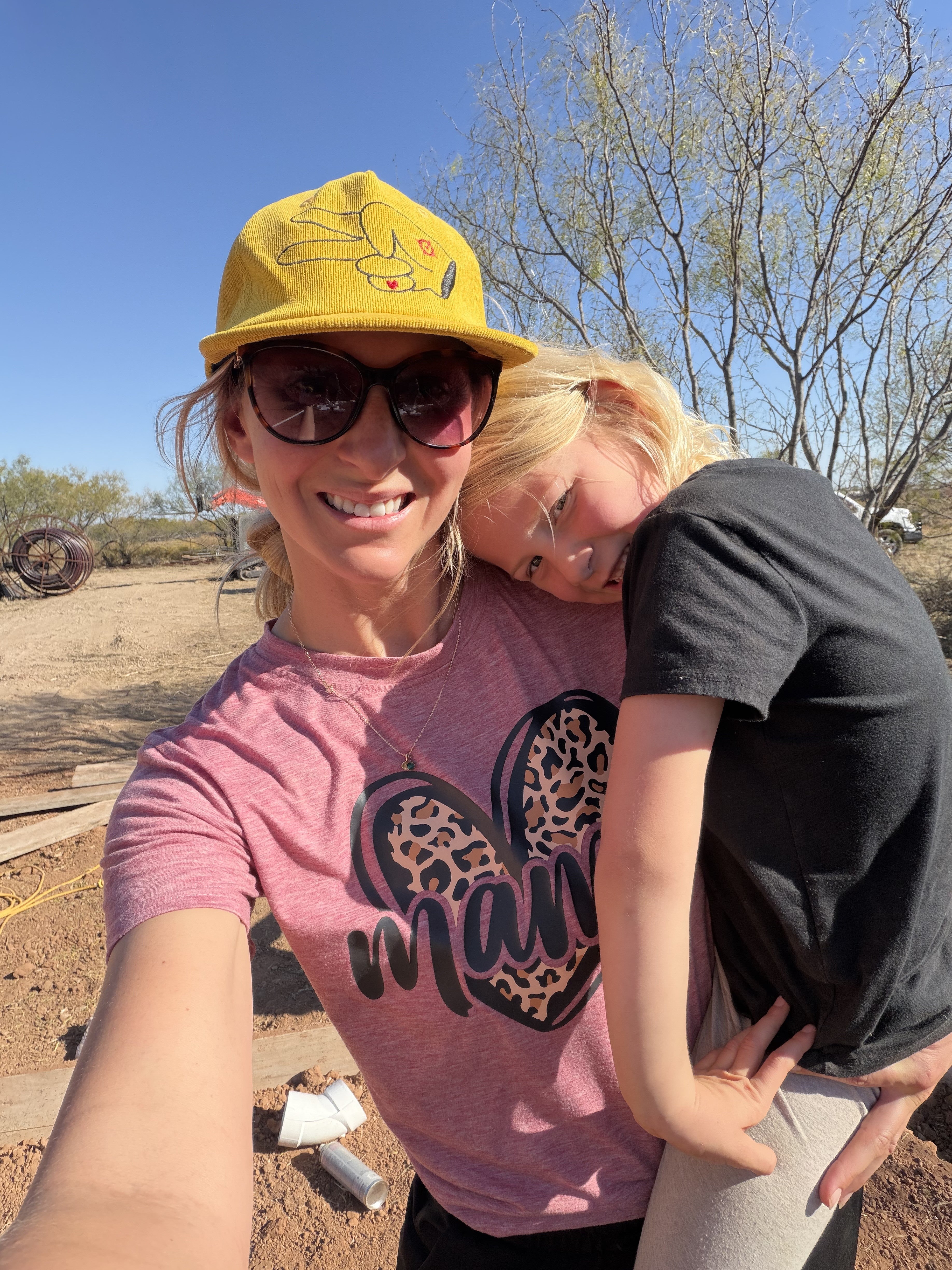Lifestyle photo of a woman wearing a Hustlin Hippie mustard corduroy snapback hat while holding her daughter outdoors in the sunshine.