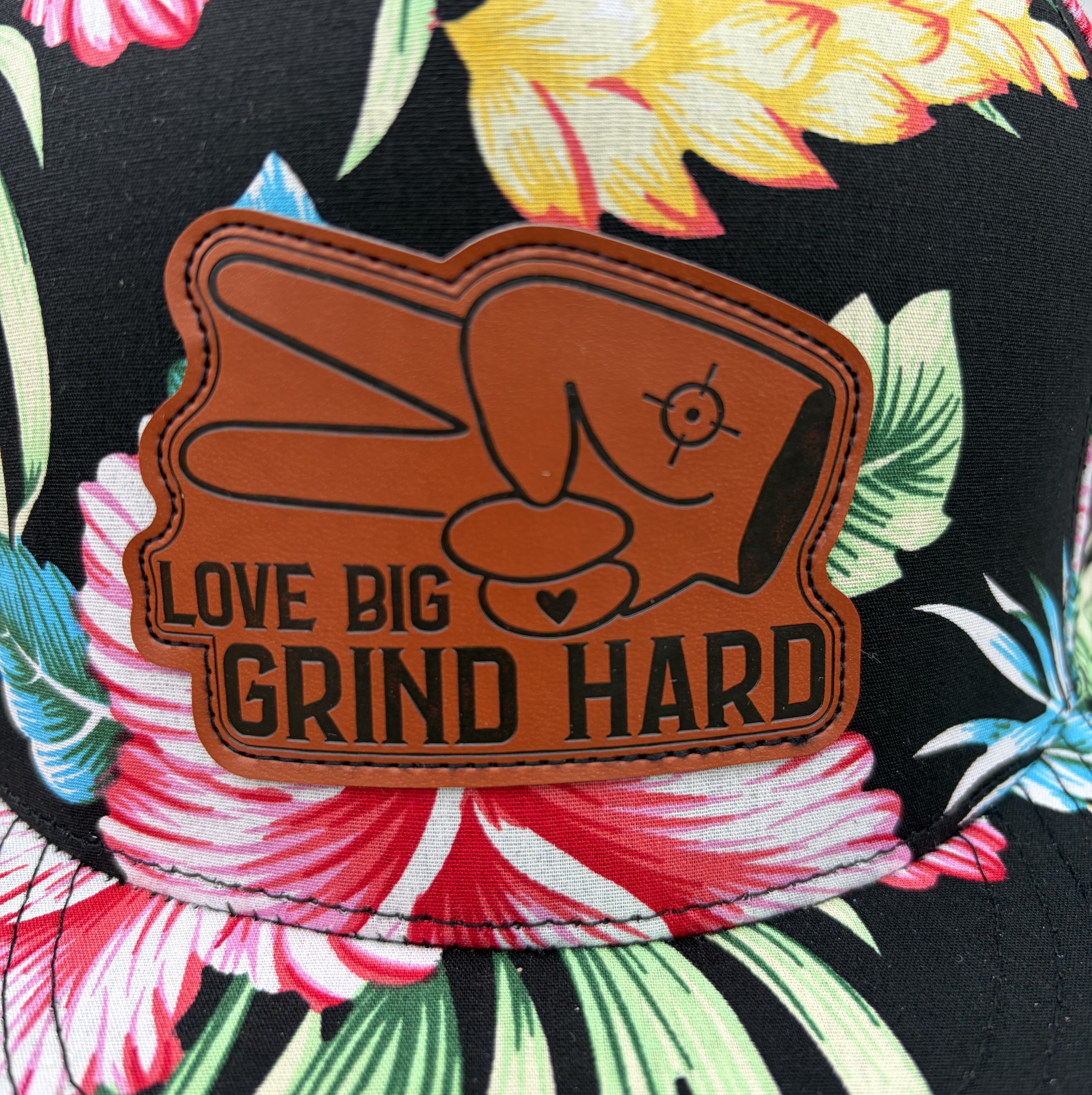 Close-up of Love Big Grind Hard leather patch on tropical floral flat bill snapback hat.