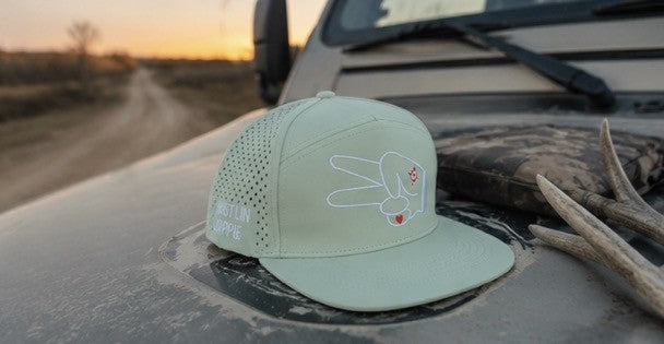Mint green Hustlin Hippie hydro snapback displayed on a truck hood beside antlers on a country backroad.