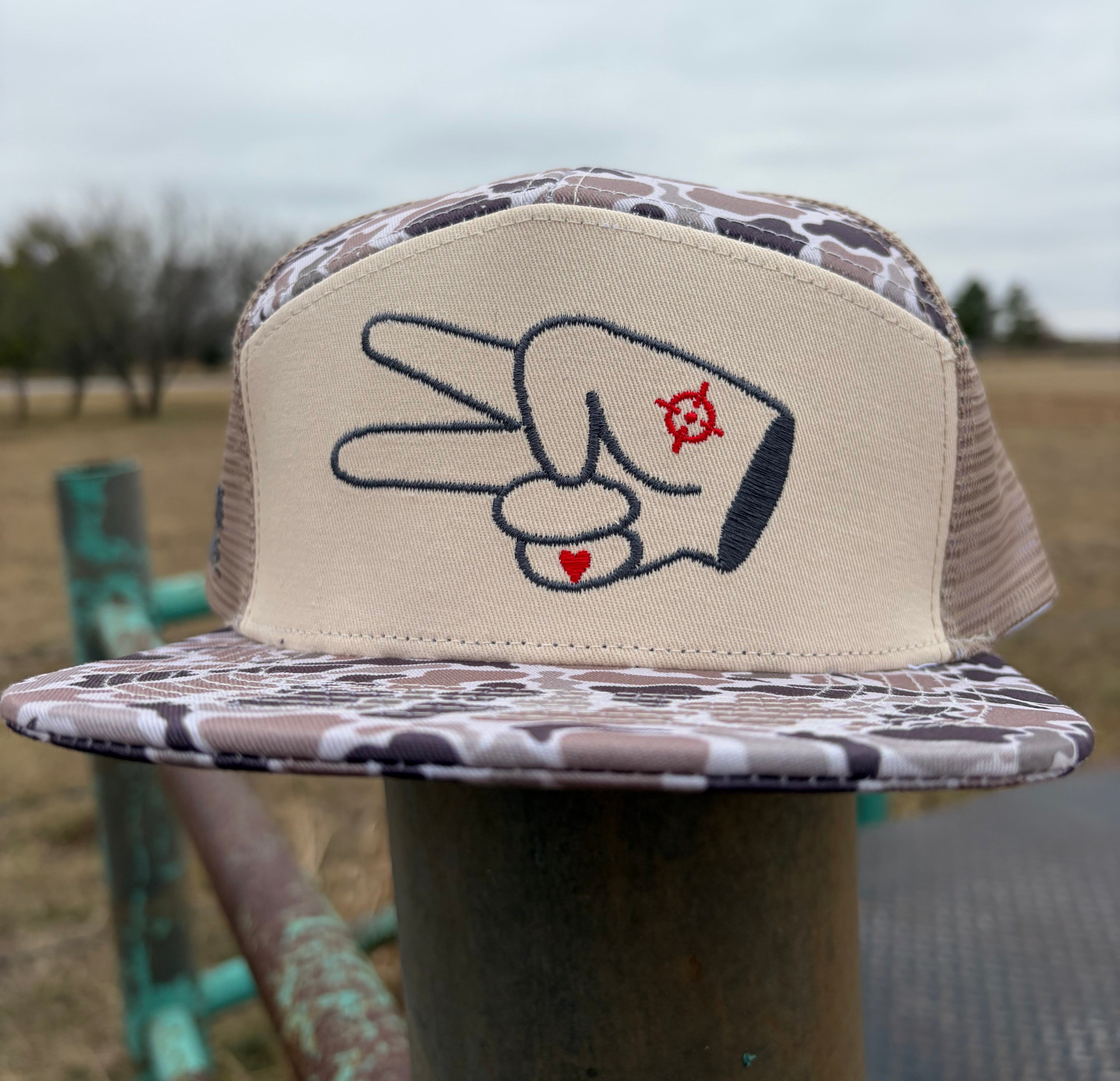 Front-facing view of Hustlin Hippie tan camo mesh back trucker hat with embroidered signature hand logo