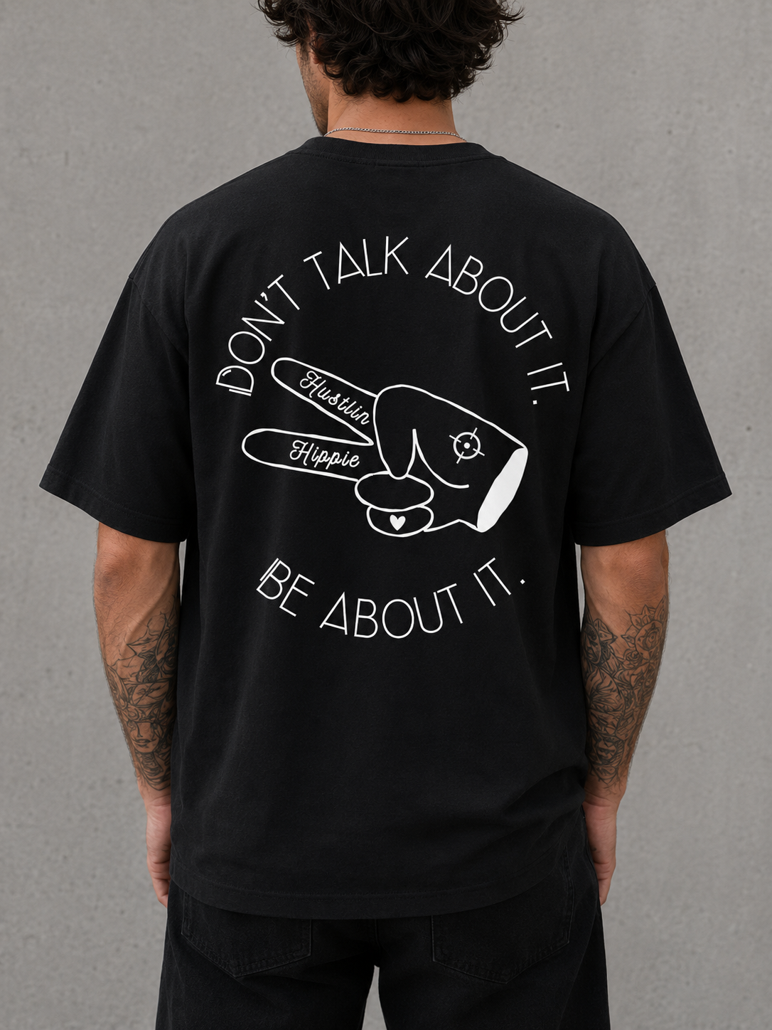 Back view of black Hustlin Hippie ‘BE ABOUT IT’ t-shirt with large white graphic and slogan design