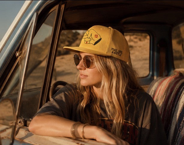 Woman leaning out of a vintage truck window wearing a mustard yellow Hustlin Hippie corduroy flat bill hat.