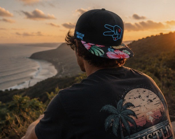 Lifestyle image of a Hustlin Hippie floral brim snapback hat overlooking the ocean at sunset with tropical coastal views.