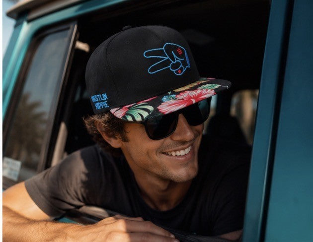 Close-up lifestyle photo of a black Hustlin Hippie floral brim snapback hat worn while leaning out of an adventure vehicle.