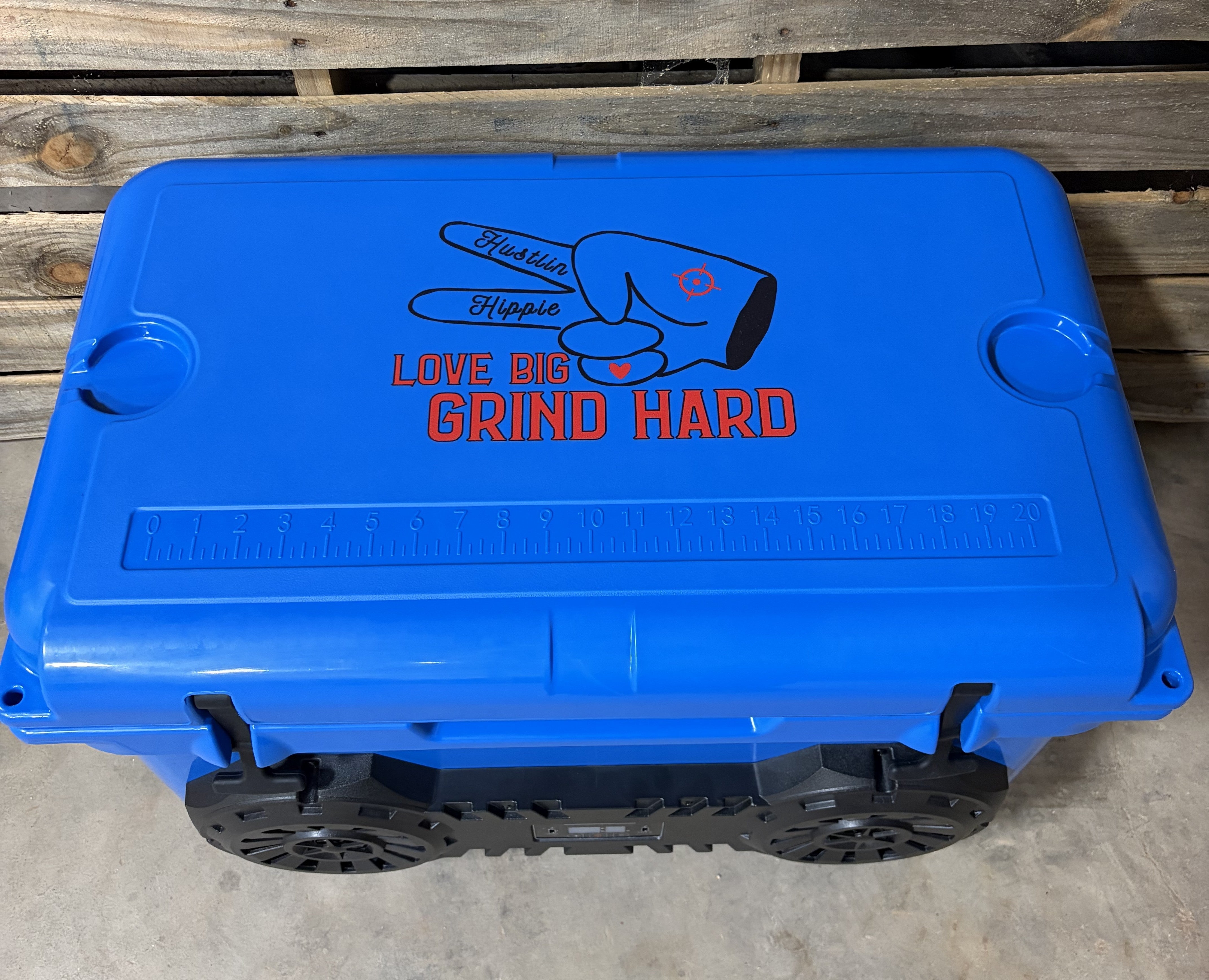 Top-down view of Blue Hound Boxx speaker cooler lid featuring integrated measuring ruler, molded cup holders and signature "Love Big, Grind Hard" branding