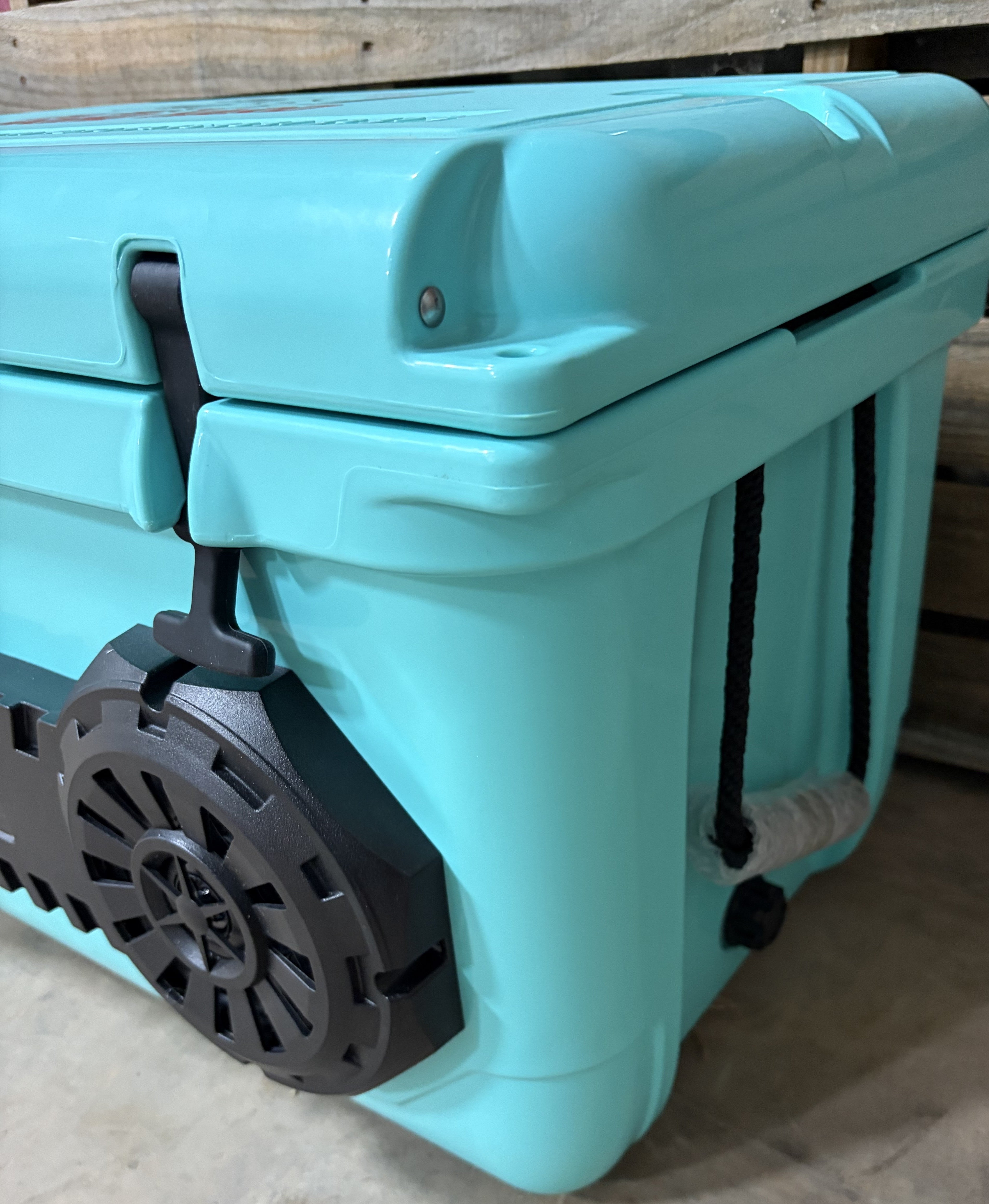 Side angle view of teal Hound Boxx Bluetooth cooler speaker featuring roto-molded body, integrated speaker system, rope side handle and drain plug detail