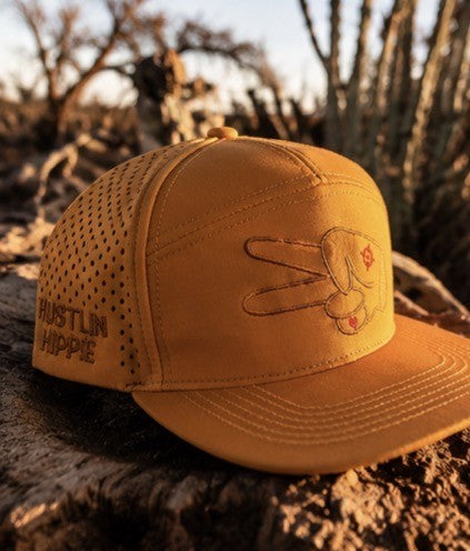 Golden burnt orange Hustlin Hippie hydro snapback hat styled outdoors at a rugged campsite with warm sunset lighting and backroads adventure vibes.