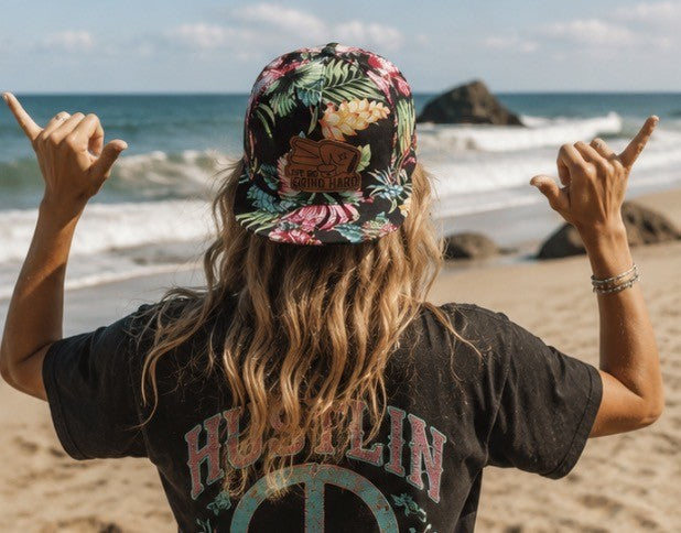 Woman wearing Hustlin Hippie Love Big Grind Hard floral snapback hat overlooking the ocean at sunset beach lifestyle scene