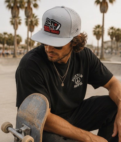 Man wearing gray Love Big Grind Hard hydro snapback hat at skatepark with modern streetwear vibe.