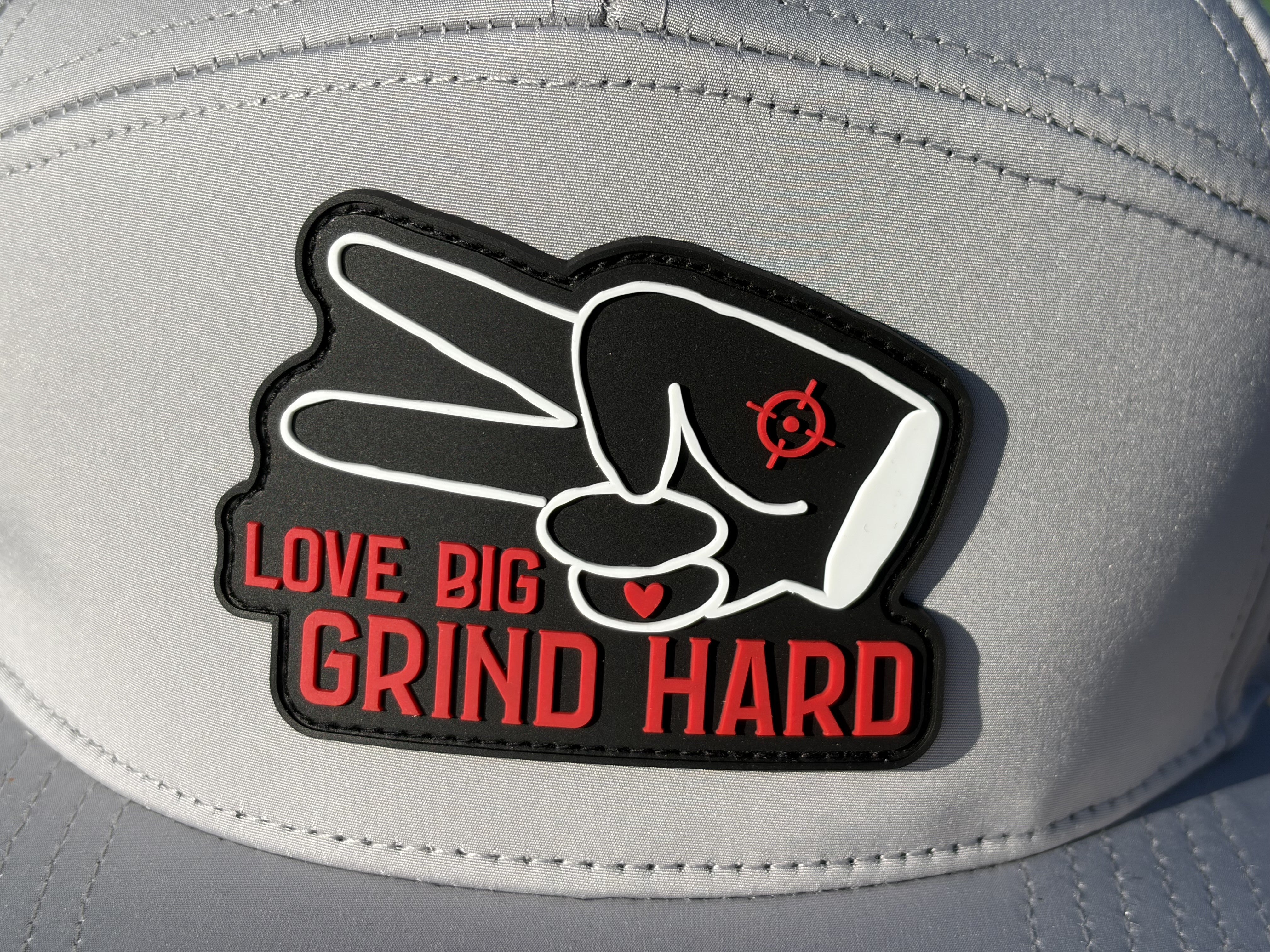 Close-up of Hustlin Hippie Love Big Grind Hard rubber patch on gray hydro performance snapback hat