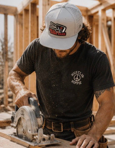 Construction worker wearing gray Love Big Grind Hard hydro snapback hat while cutting lumber on a framing jobsite