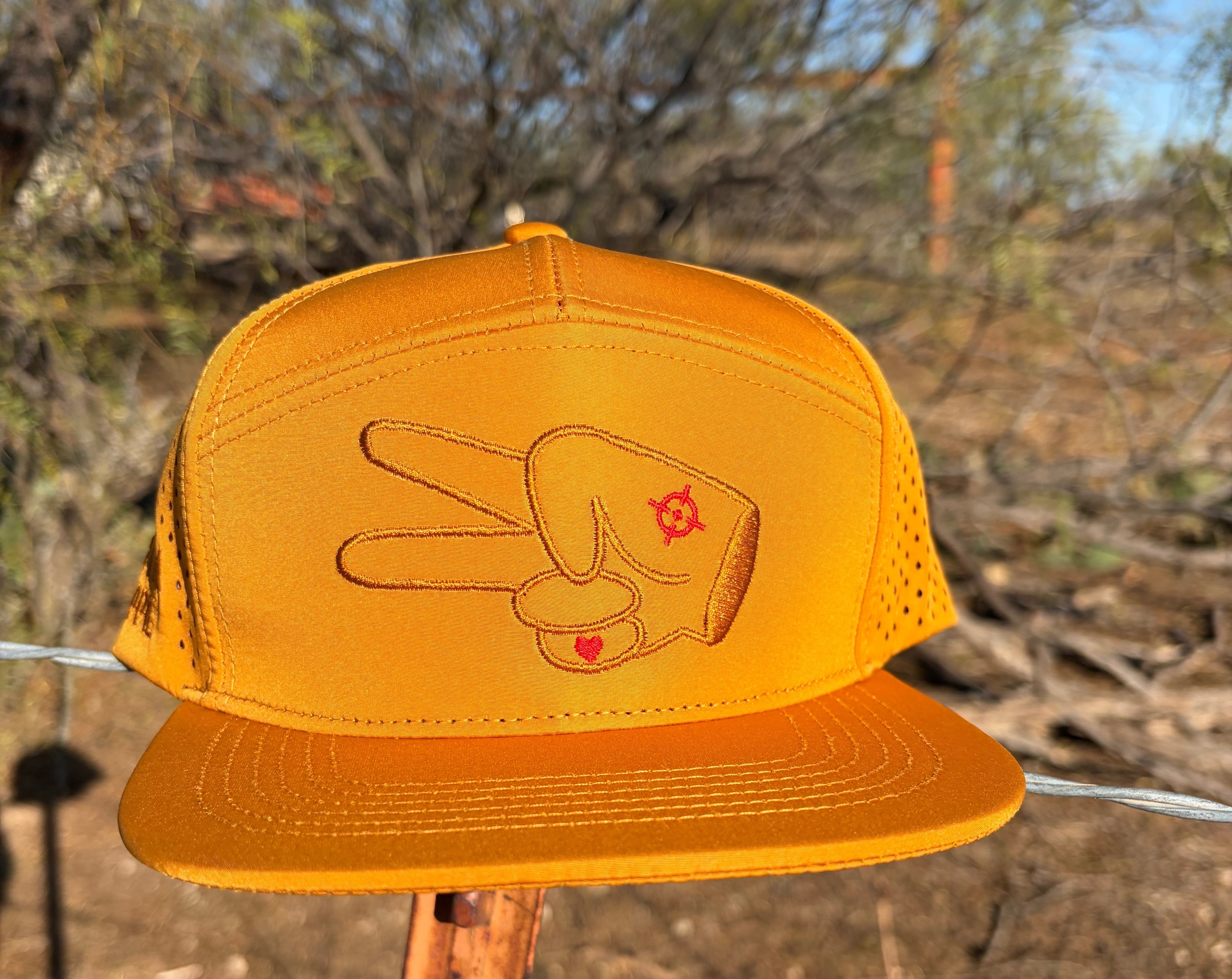 Front view of Hustlin Hippie Signature Burnt Orange Hydro Snapback Hat with embroidered signature hand logo and laser perforated side panels outdoors in rugged backroads setting