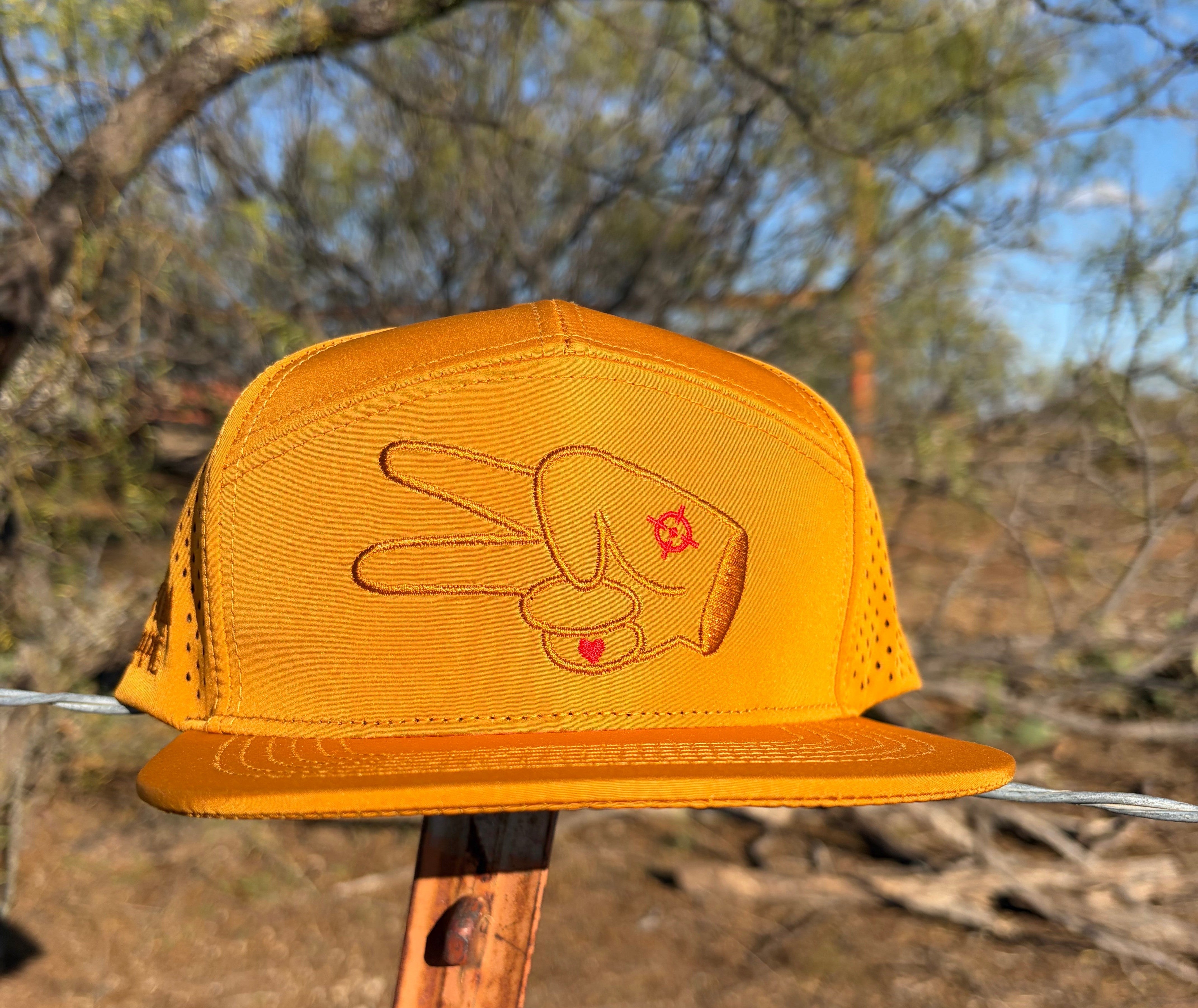 Front view of Hustlin Hippie Signature Burnt Orange Hydro Snapback flat bill hat with embroidered signature hand logo and perforated performance panels in outdoor hunting-inspired setting