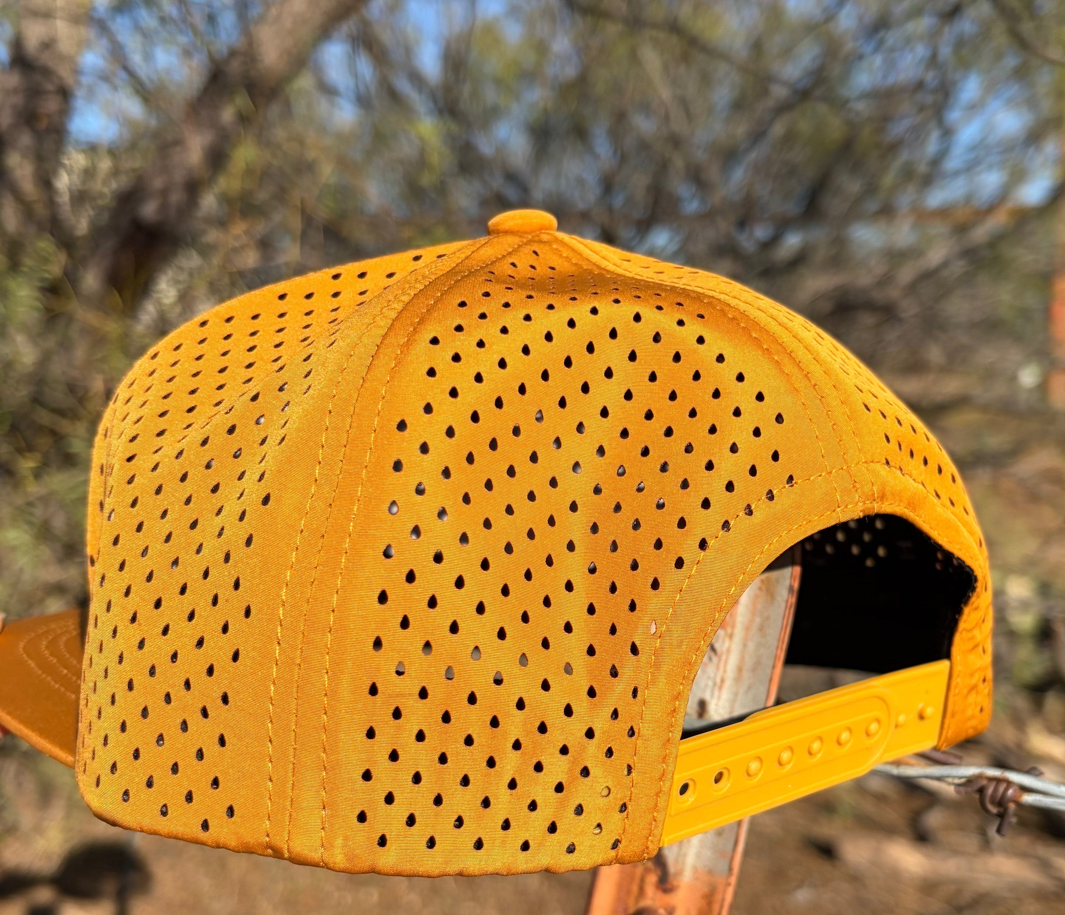 Rear view of Hustlin Hippie Signature Burnt Orange Hydro Snapback Hat showing laser perforated hydro performance material and adjustable snapback closure outdoors in rugged landscape