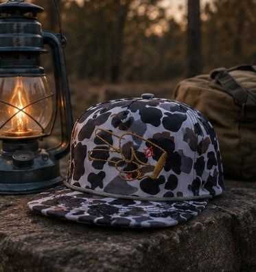 Hustlin Hippie Signature Midnight Camo snapback hat beside a lantern at a rustic campsite during sunset.