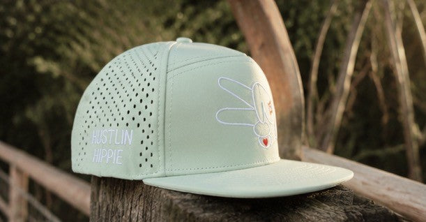 Signature Mint Green Hydro Snapback Hat resting on a wooden rail during golden hour with peaceful outdoor scenery.
