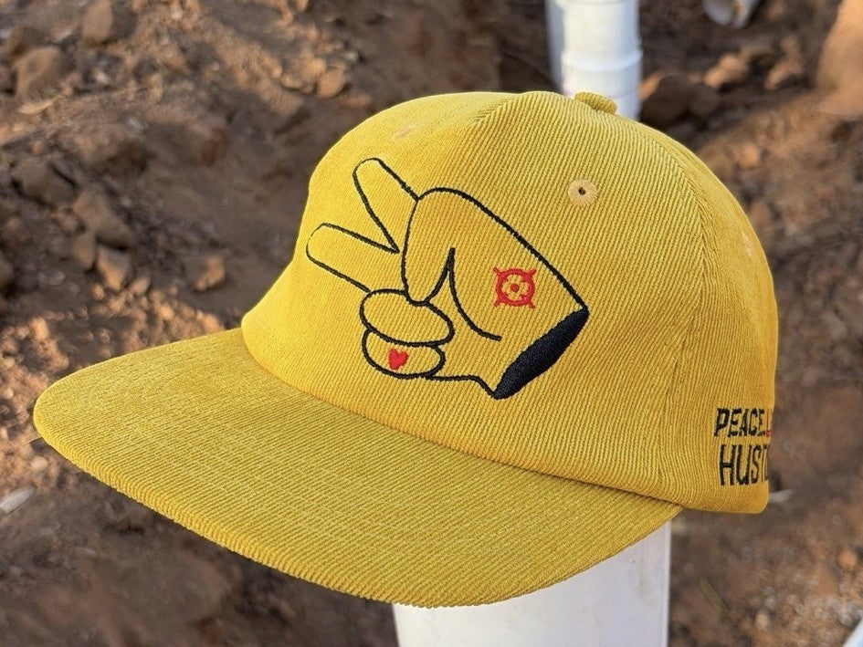 Angled view of a mustard yellow Hustlin Hippie corduroy flat bill snapback hat with embroidered signature hand logo.