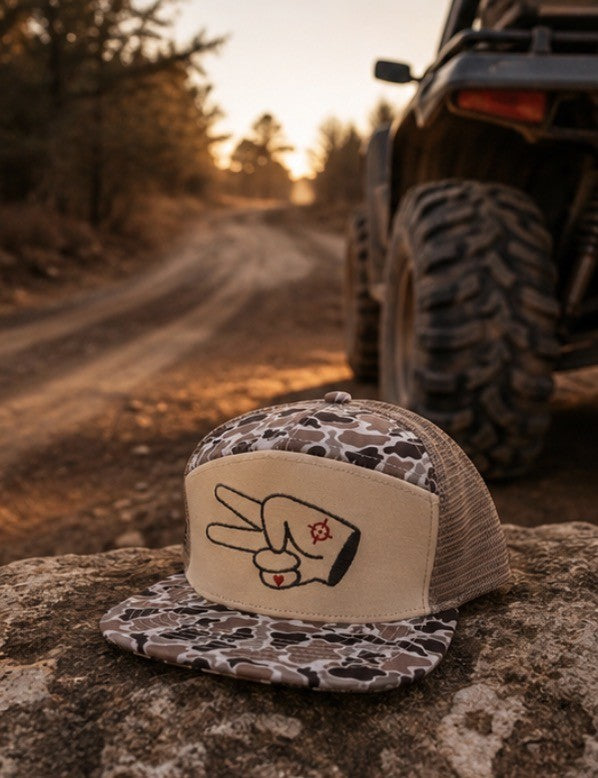 Signature Tan Camo Mesh Back Trucker Hat beside off-road UTV on dusty backroads at sunset