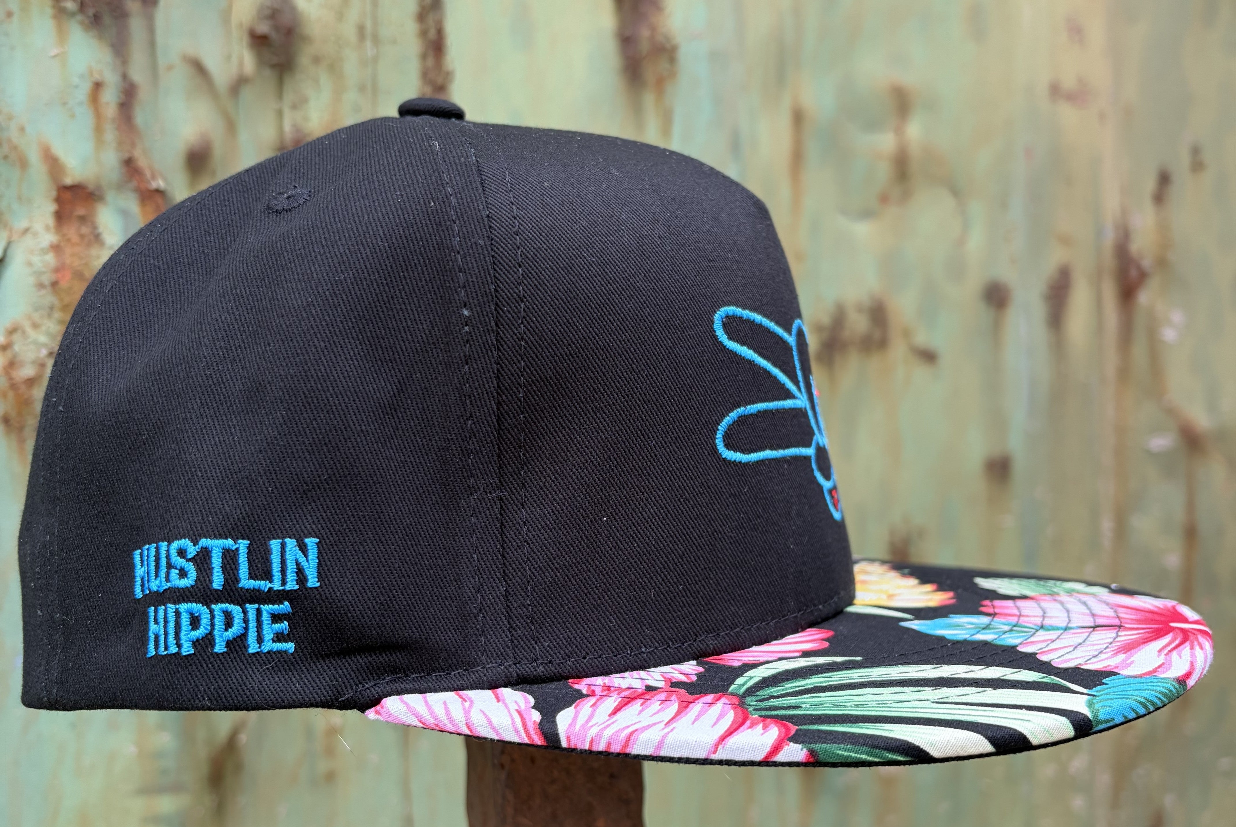 Side profile of the Hustlin Hippie Signature Tropical Floral snapback hat with blue embroidered branding and colorful floral flat bill.